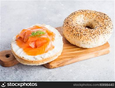 Fresh healthy bagel sandwich with salmon, ricotta and dill on vintage chopping board on light kitchen table background.