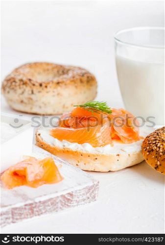 Fresh healthy bagel sandwich with salmon, ricotta and glass of milk on light kitchen table background.