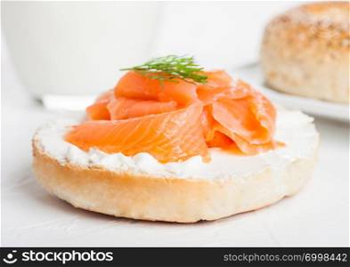 Fresh healthy bagel sandwich with salmon, ricotta and glass of milk on light kitchen table background.