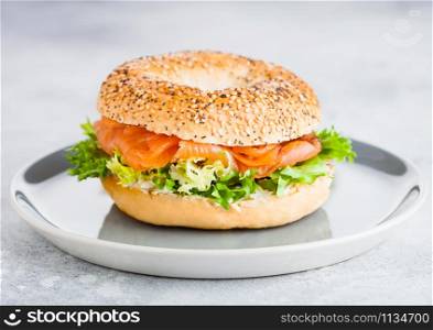 Fresh healthy bagel sandwich with salmon, ricotta and lettuce in grey plate on light kitchen table background.