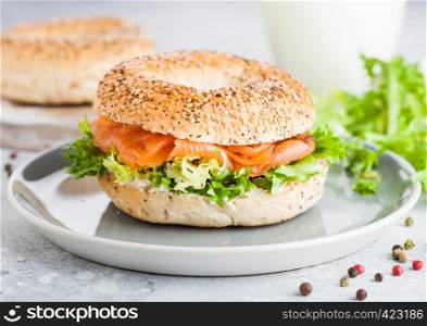 Fresh healthy bagel sandwich with salmon, ricotta and lettuce in grey plate on light kitchen table background. Healthy diet food.