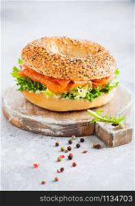 Fresh healthy bagel sandwich with salmon, ricotta and lettuce on vintage chopping board on white kitchen table background.