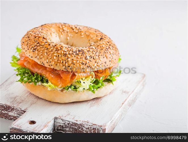 Fresh healthy bagel sandwich with salmon, ricotta and lettuce on vintage chopping board on stone kitchen table background.