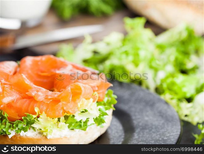 Fresh healthy bagel sandwich with salmon, ricotta and soft egg on vintage chopping board on white kitchen table background