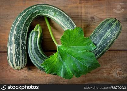 Fresh healthy green zucchini courgettes in brown wooden background