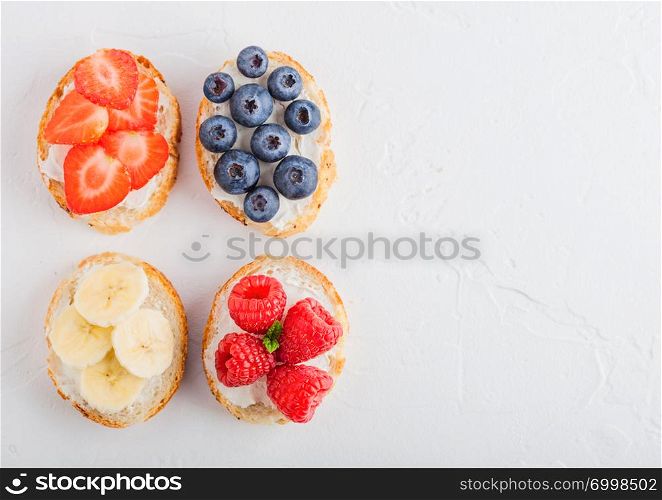 Fresh healthy mini sandwiches with cream cheese, fruits and berries. Strawberries, blueberries, bananas and raspberries on stone kitchen table background. Space for text.