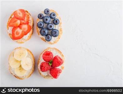 Fresh healthy mini sandwiches with cream cheese, fruits and berries. Strawberries, blueberries, bananas and raspberries on stone kitchen table background. Space for text.