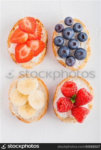 Fresh healthy mini sandwiches with cream cheese, fruits and berries. Strawberries, blueberries, bananas and raspberries on stone kitchen table background.