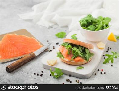 Fresh healthy organic sandwich with bagel and salmon, cream cheese and wild rocket on chopping board with smoked salmon pack on light.