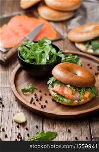 Fresh healthy organic sandwich with bagel and salmon, cream cheese and wild rocket in bowl with bread and smoked salmon pack on wooden background.