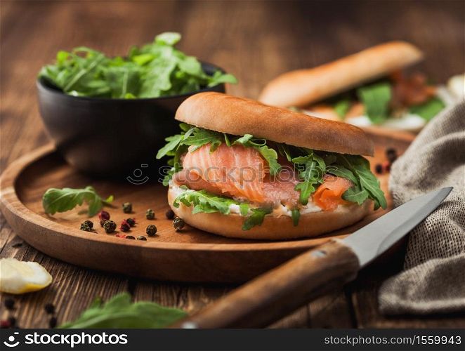 Fresh healthy organic sandwich with salmon and bagel, cream cheese and wild rocket in wooden plate with knife and towel.