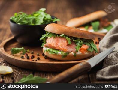 Fresh healthy organic sandwich with salmon and bagel, cream cheese and wild rocket in wooden plate with knife and towel.