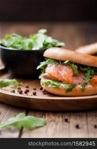 Fresh healthy organic sandwich with salmon and bagel, cream cheese and wild rocket in plate on wooden background.