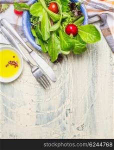 Fresh healthy salad with lettuce , cherry tomatoes and radish on light rustic background with cutlery and olive oil, top view, place for text. Healthy lifestyle or detox diet food concept