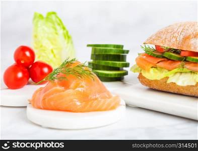 Fresh healthy salmon sandwich with lettuce and cucumber and tomatoes on marble board on white marble background.Diet healthy food