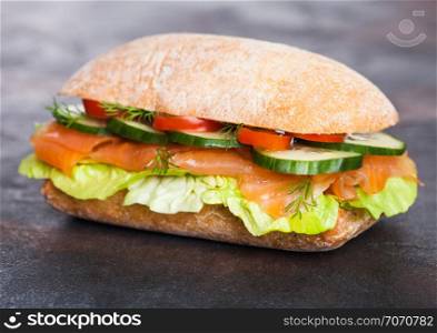 Fresh healthy salmon sandwich with lettuce and cucumber on black stone background. Breakfast snack