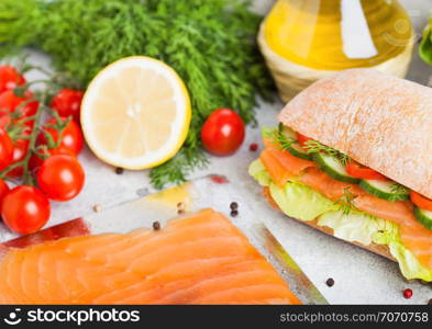 Fresh healthy salmon sandwich with lettuce and cucumber on the plate on stone background. Breakfast snack. Fresh tomatoes, dill and lemon.