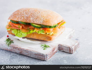 Fresh healthy salmon sandwich with lettuce and cucumber on vintage chopping board on white stone background. Breakfast snack