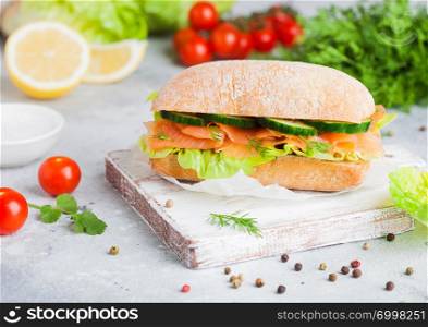 Fresh healthy salmon sandwich with lettuce and cucumber on vintage chopping board on stone background. Breakfast snack. Fresh tomatoes, dill and lemon.