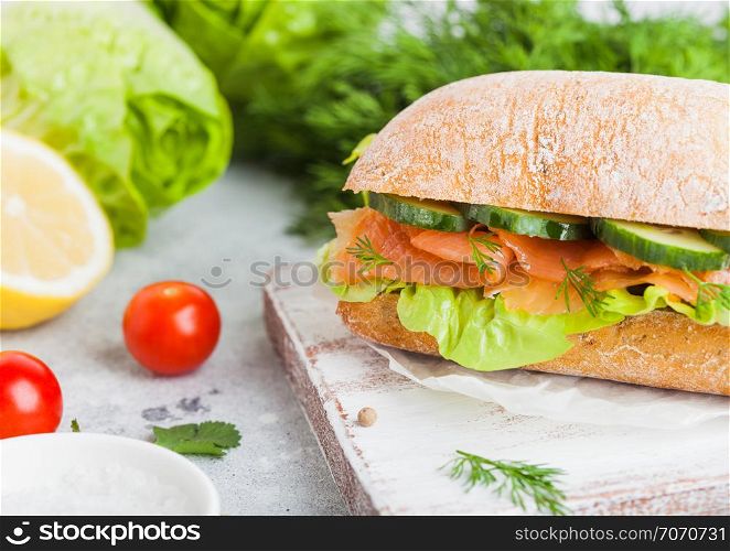 Fresh healthy salmon sandwich with lettuce and cucumber on vintage chopping board on stone background. Breakfast snack. Fresh tomatoes, dill and lemon.