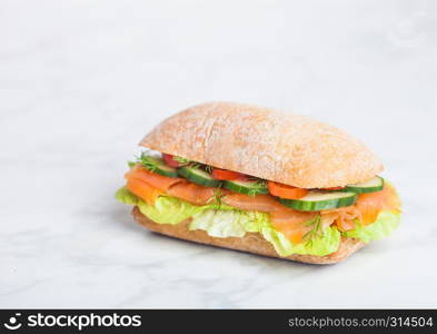 Fresh healthy salmon sandwich with lettuce and cucumber on white stone background. Breakfast snack