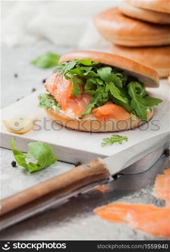 Fresh healthy sandwich with salmon and bagel, cream cheese and wild rocket with knife on white table background.
