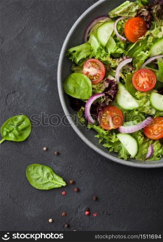 Fresh healthy vegetarian vegetables salad with tomatoes and cucumber, red onion and spinach in large grey bowl plate on dark background. Top view. Macro