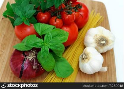 Fresh herbs and vegetables to make spaghetti, including red onion, tomatoes, basil, oregano, garlic and dry pasta.. Raw Spaghetti Ingredients