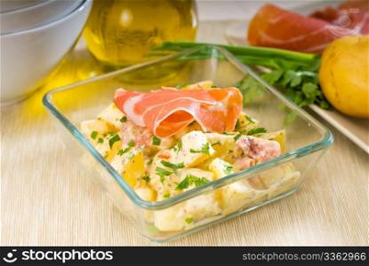 fresh home made parma ham and potato salad,with raw ingredients around with bowls and dishware on a table