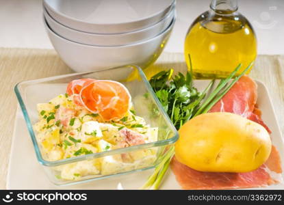 fresh home made parma ham and potato salad,with raw ingredients around with bowls and dishware on a table