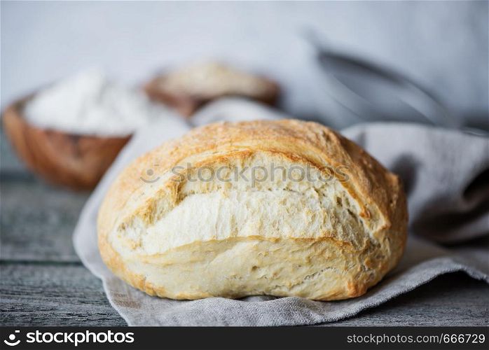 Fresh homemade bread covered with gray linen napkin lie on the background of old wooden boards