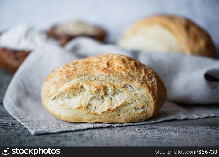 Fresh homemade bread covered with gray linen napkin lie on the background of old wooden boards