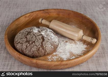 Fresh homemade bread made from durum wheat, rye, on a wooden tray with a rolling pin. Composition on a beautiful tablecloths canvas. Photos for magazines about cooking, confectionery, cooking.