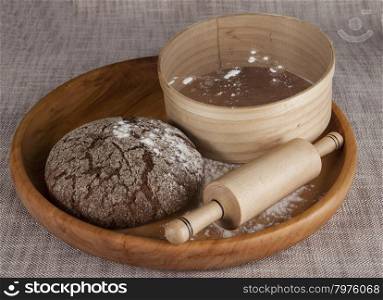 Fresh homemade bread made from durum wheat, rye, on a wooden tray with a sieve for flour and a rolling pin. Composition on a beautiful tablecloths canvas. Photos for magazines about cooking, confectionery, cooking.