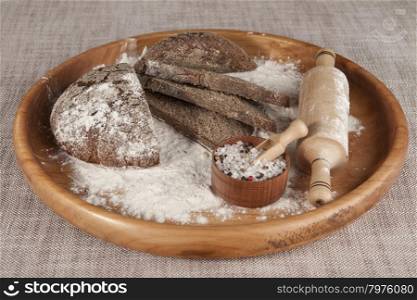 Fresh homemade bread made from durum wheat, rye, on a wooden tray with a jar of salt. Composition on a beautiful tablecloths canvas. Photos for magazines about cooking, confectionery, cooking.