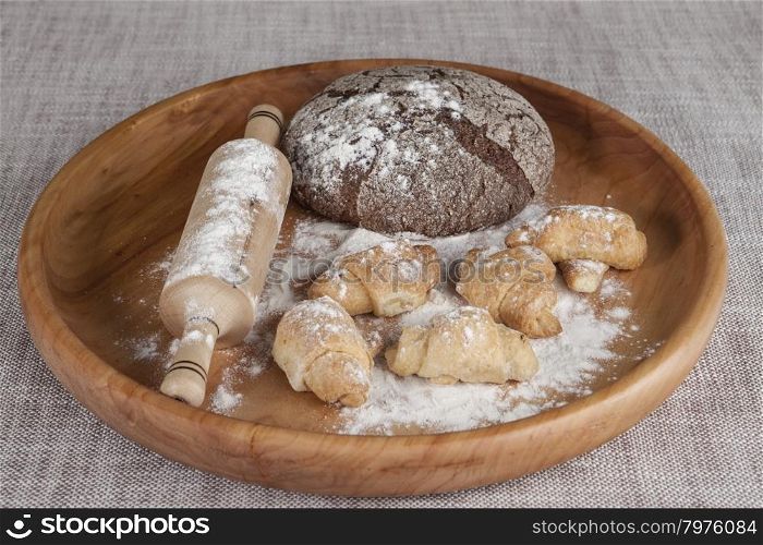 Fresh homemade bread made from durum wheat, rye, on a wooden tray with a rolling pin and pastry rolls with jam . Composition on a beautiful tablecloths canvas. Photos for magazines about cooking.