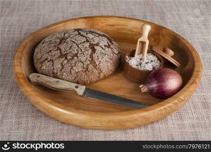 Fresh homemade bread made from durum wheat, rye, on a wooden tray with a jar of salt, a knife and onion. Composition on a beautiful tablecloths canvas. Photos for magazines about cooking, confectionery, cooking.