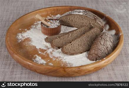 Fresh homemade bread made from durum wheat, rye, on a wooden tray with a jar of salt. Composition on a beautiful tablecloths canvas. Photos for magazines about cooking, confectionery, cooking.