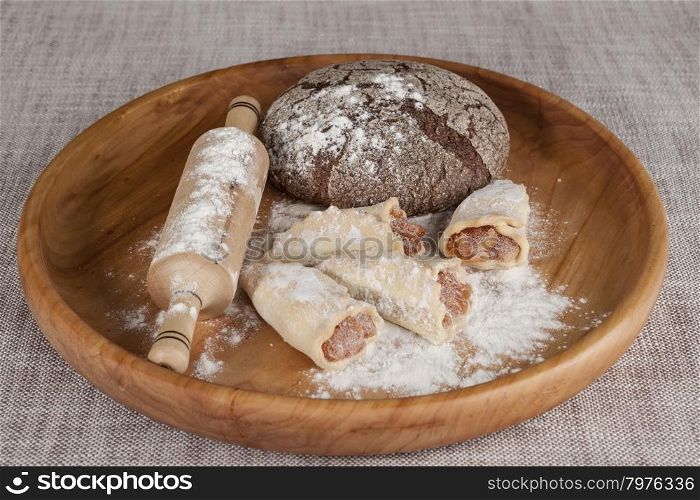 Fresh homemade bread made from durum wheat, rye, on a wooden tray with a rolling pin and pastry rolls with jam . Composition on a beautiful tablecloths canvas. Photos for magazines about cooking.