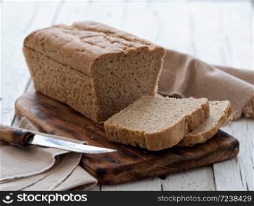 Fresh homemade bread, partially sliced. Bread is located on a wooden surface. Near napkins and a knife. White wood background. Close-up. The concept for baking.