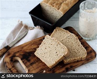 Fresh homemade bread, partially sliced. Bread is located on a wooden surface. Near napkins and a knife. Jar with yeast. White wood background. Close-up. The concept for baking.