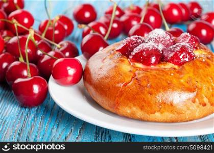 Fresh homemade bun with sweet cherry in a white dish on a blue wooden background