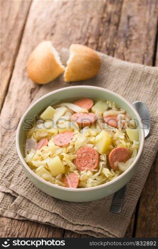 Fresh homemade cabbage, potato and sausage stew in bowl, with bread roll and spoon on the side (Selective Focus, Focus one third into the dish). Cabbage, Potato and Sausage Stew