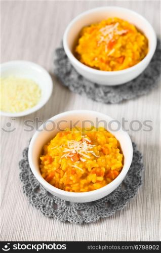 Fresh homemade carrot risotto made with pureed carrot and roasted carrot pieces, garnished with grated cheese, photographed with natural light (Selective Focus, Focus in the middle of the first risotto)