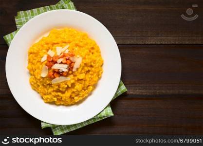 Fresh homemade carrot risotto made with pureed carrot, garnished with roasted carrot and hard cheese, photographed overhead on dark wood with natural light (Selective Focus, Focus on the risotto)