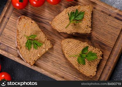 Fresh homemade chicken liver pate on bread over grey background. Appetizer, baguette with liver paste and herbs, closeup. Homemade breakfast
