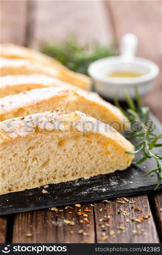 fresh homemade ciabatta bread sliced on stone slate board, olive oil and rosemary on wooden background