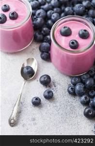 Fresh homemade creamy blueberry yoghurt with fresh blueberries and silver spoon on stone table background