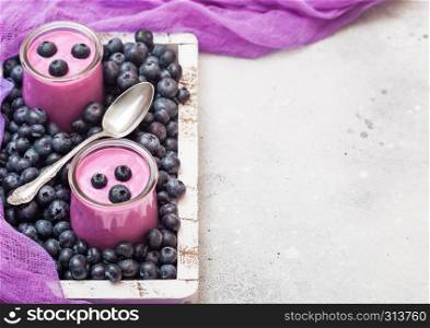 Fresh homemade creamy blueberry yoghurt with fresh blueberries in vintage wooden box and silver spoon on stone table background