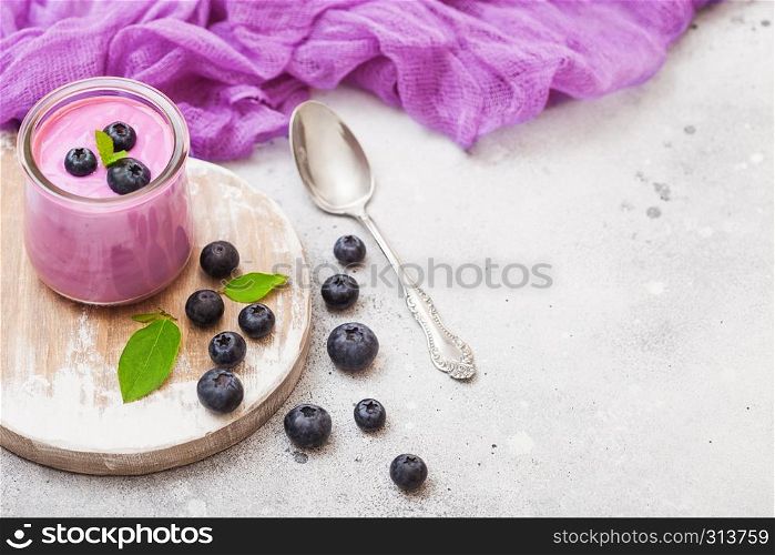 Fresh homemade creamy blueberry yoghurt with fresh blueberries on vintage wooden board and silver spoon on stone table background